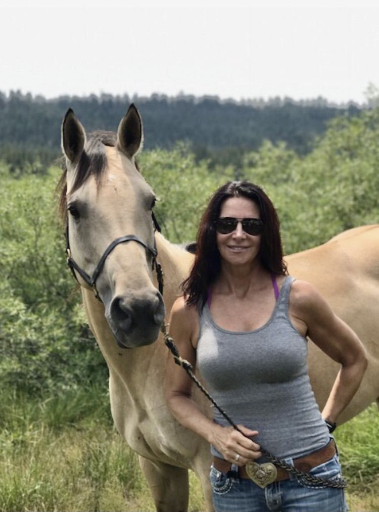 A woman standing next to a horse in the grass.